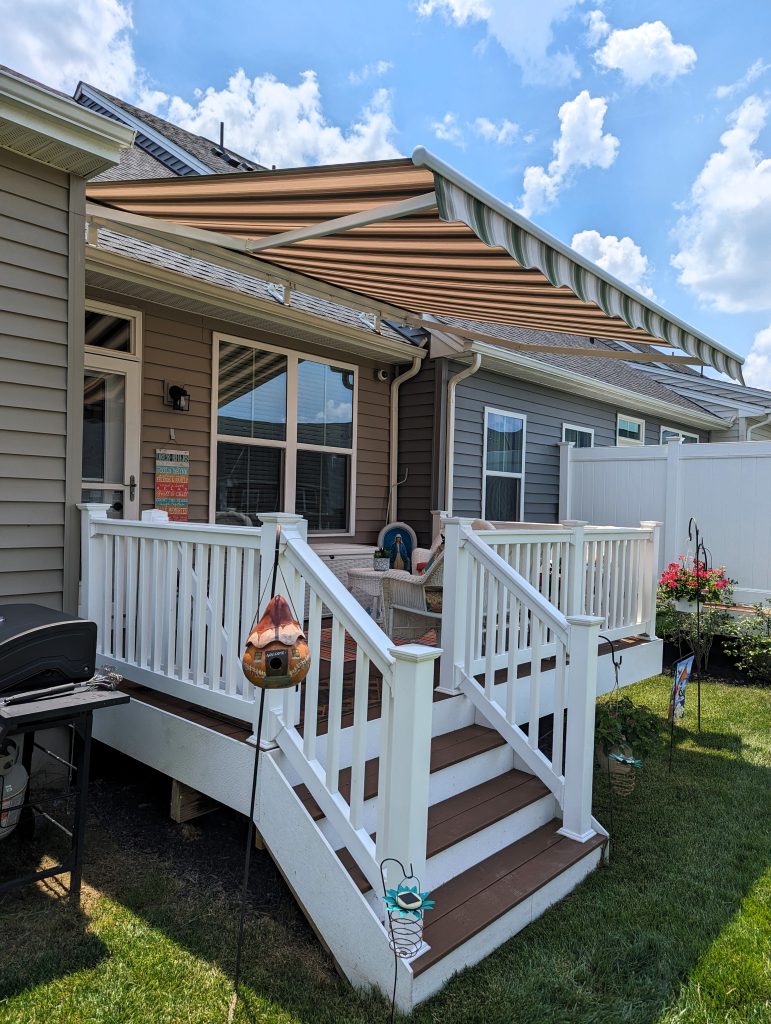 Small back deck with white railings, brown flooring, and a white and green fabric awning.